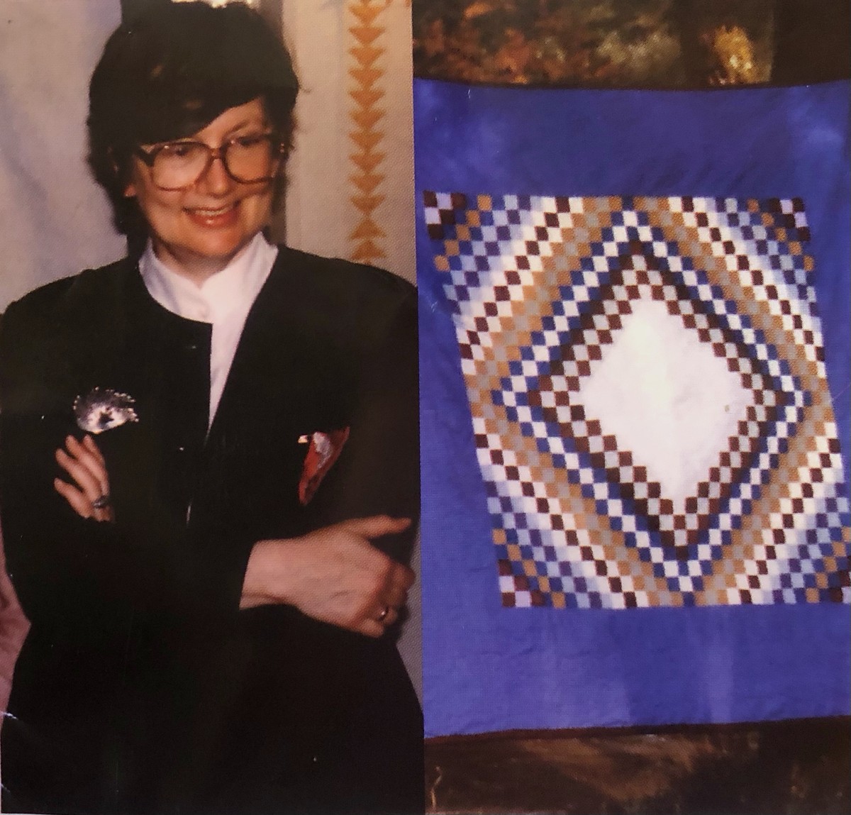 A. Barbara Horvàth-Storms in dunklem Jackett vor einem kornblumenblauen Trip-around-the-World-Quilt, dessen Rautenfeld aus Braun, Ocker, Blau und Weiss sich zu einer hellen Mitte öffnet.